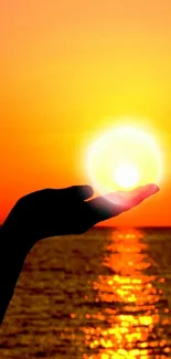 Hand holding the sun with ocean sunset background.