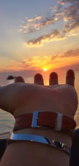 Hand reaching towards a vibrant sunset over the ocean.