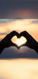 Hands forming a heart shape against a beautiful sunset backdrop.