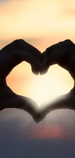 Silhouette of hands in heart shape against sunset.