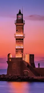 Lighthouse against purple sunset sky over ocean.