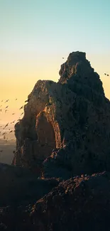 Mountain peak at sunset with birds flying in the orange sky.