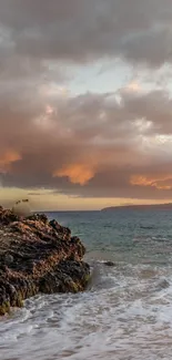 Stunning sunset over a rocky ocean shore with dramatic clouds.