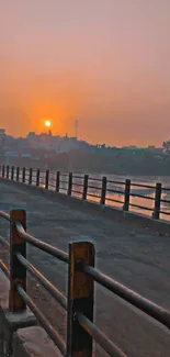 Orange sunset over a city bridge with water reflections.