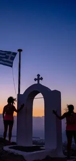 Silhouetted figures and a Greek flag against a sunset backdrop.