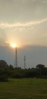 Beautiful sunset over green fields with silhouetted trees and towers.