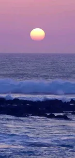 Pink sunset over ocean with waves crashing on the rocky shore.