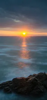 Beautiful sunset over the ocean with a rocky shore in the foreground.