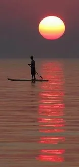 A solitary paddleboarder under a vibrant sunset on calm waters.