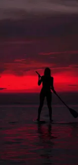 Silhouette of a paddleboarder against a crimson sunset over tranquil waters.