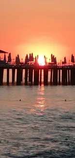 Sunset over the ocean with a pier silhouetted against an orange sky.