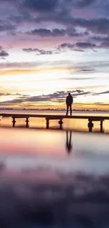 Silhouette on a dock with sunset reflection over water and vibrant evening sky.