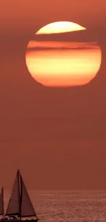 A sailboat glides across the ocean under a fiery sunset sky.