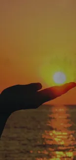 Hand silhouetted against a sunset over the ocean, with golden hues.