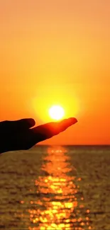 Silhouette of a hand holding the glowing sun during a serene beach sunset.