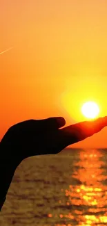 Silhouette of hand holding a sunset over the ocean.