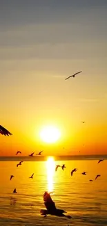 Golden sunset over ocean with birds flying in serene sky.