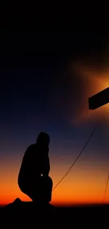 Silhouette kneeling at cross during a sunset.