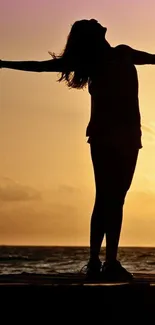 Silhouette of a person embracing sunset by the sea, blending orange and purple hues.