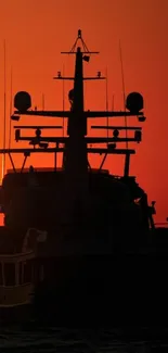 Silhouette of boat at sunset with orange sky.