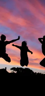 Silhouette figures jumping at sunset with vibrant sky.