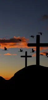 Silhouetted crosses at sunset with birds flying and scenic mountains.