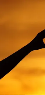 Silhouette forming a heart shape against a vivid orange sunset.