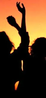 Silhouetted figures dance against a vibrant orange sunset sky.