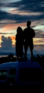 Silhouetted couple on van roof at sunset.