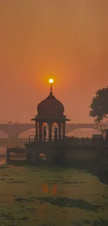 Silhouette structure against a vibrant sunset over a river.