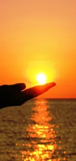 Hand silhouette holding the sun at sunset over the ocean.