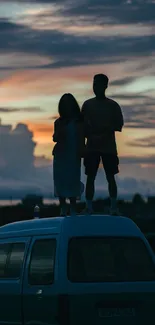 Silhouetted couple stands atop a van against a colorful sunset sky.