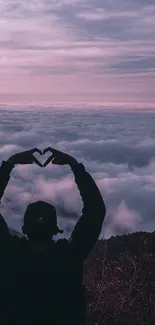 Silhouette forming heart shape in front of a vibrant sunset and clouds.