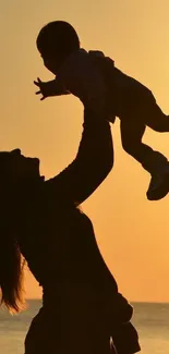 Silhouette of parent lifting child at sunset by the sea.