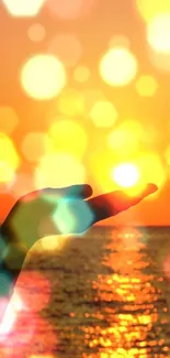 Silhouette hand holds sun against an orange sunset on the ocean.