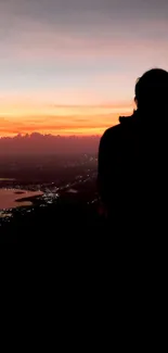 Silhouette against a vibrant orange sunset over the cityscape.