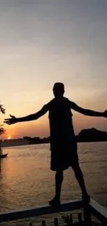 Silhouette of a person at sunset by the water, arms outstretched.