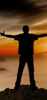 Silhouette of person embracing sunset on a misty mountain.