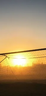 Soccer goal backlit by sunset with orange sky.