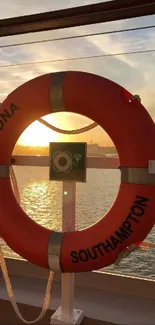 Lifebuoy ring framing a sunset on a calm ocean from a ship deck view.