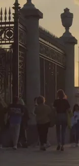 People walking by a fence during sunset in an urban area.