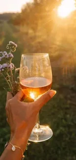 Hand holding wine glass at sunset with flowers, capturing golden hour serenity.