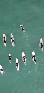 Aerial view of surfers on teal ocean waves, nine surfboards visible.