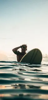 Surfer with board at ocean sunset in calm waters.