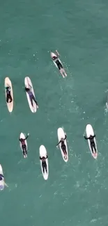 Aerial view of surfers paddling in turquoise ocean waves.