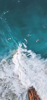 Aerial view of surfers on turquoise ocean waves crashing over rocks.