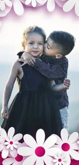 Two children embracing with floral pink border wallpaper.