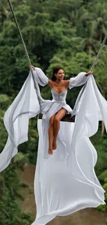 Woman swinging over lush green forest in a white dress.