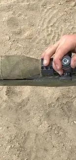 Close-up of someone adjusting a sniper scope in a sandy environment.