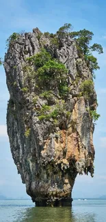 Towering limestone island under a blue sky in a tranquil ocean scene.